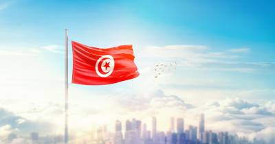 Tunisia flag wavering in beautiful clouds with building skyline. The flag with drone shot in beautiful sky. Tunisia national flag for independence day.