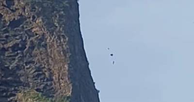 O praticante de base jump atira-se e abre o paraquedas durante a descida.