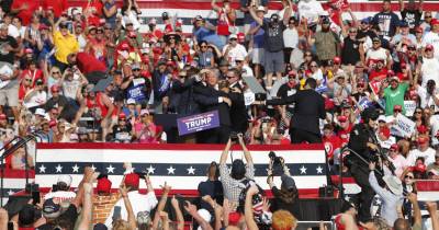 Donald Trump, de rosto ensanguentado e punho erguido, no momento em que é retirado do palco pelos agentes dos serviços secretos.